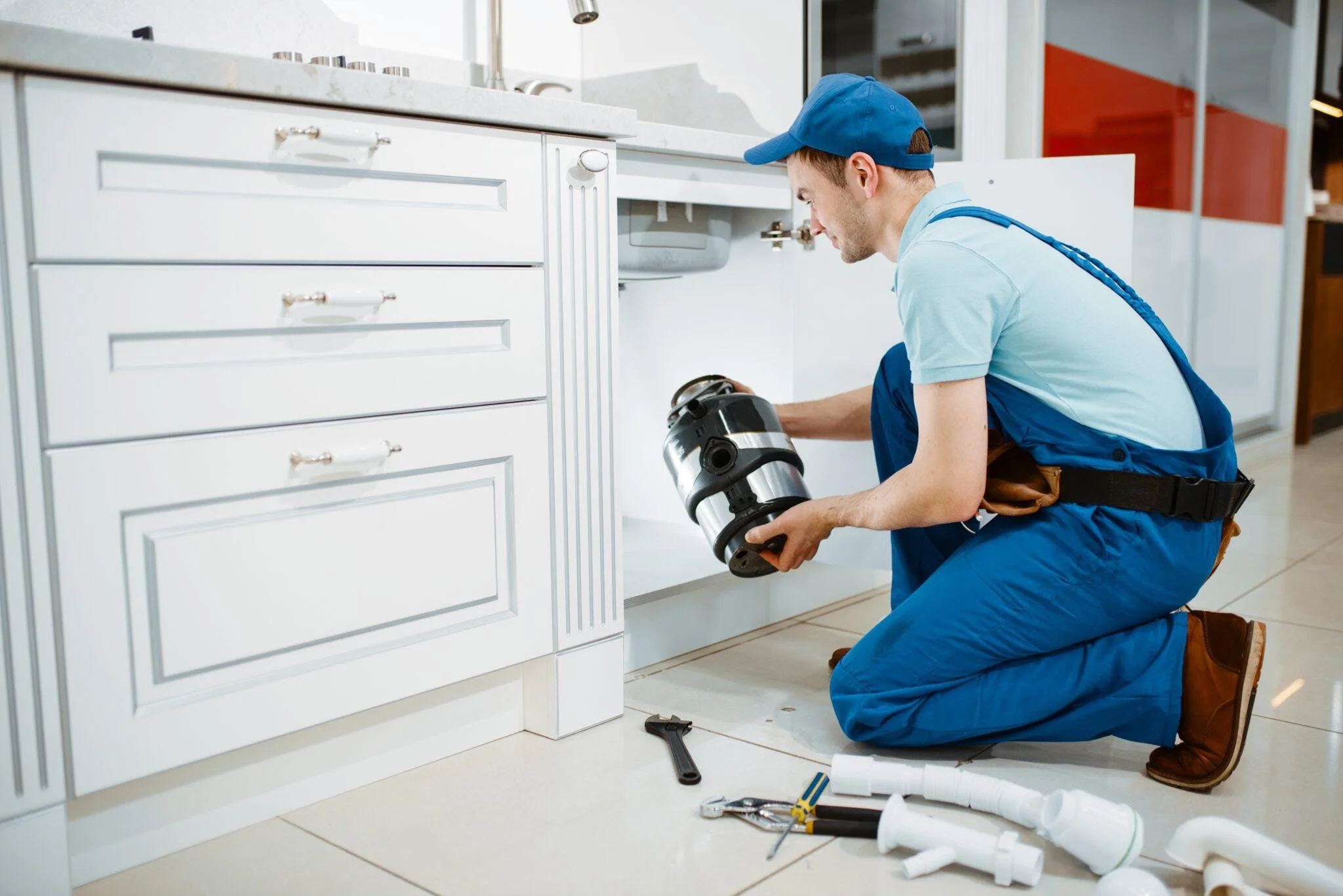 Male plumber in uniform installing disposer in the kitchen. Handywoman with toolbag repair sink, sanitary equipment service at home